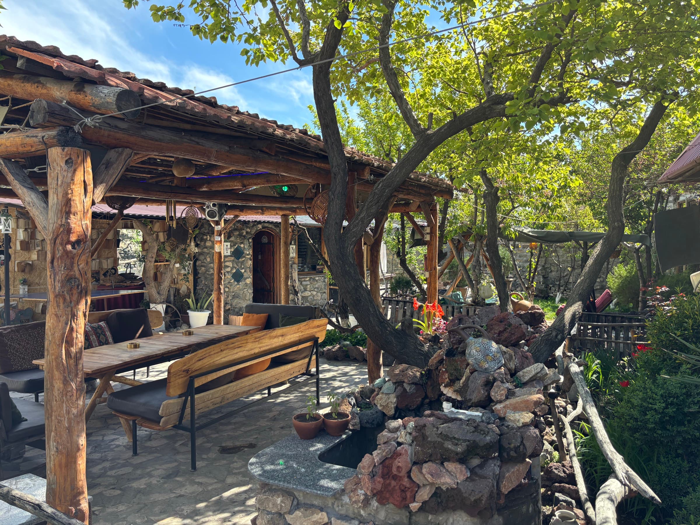 Villa Nors-ի փայտե տաղավարը՝ երկար սեղանով, նստարանով և կողքին քարերի վրայով հոսող շատրվանով