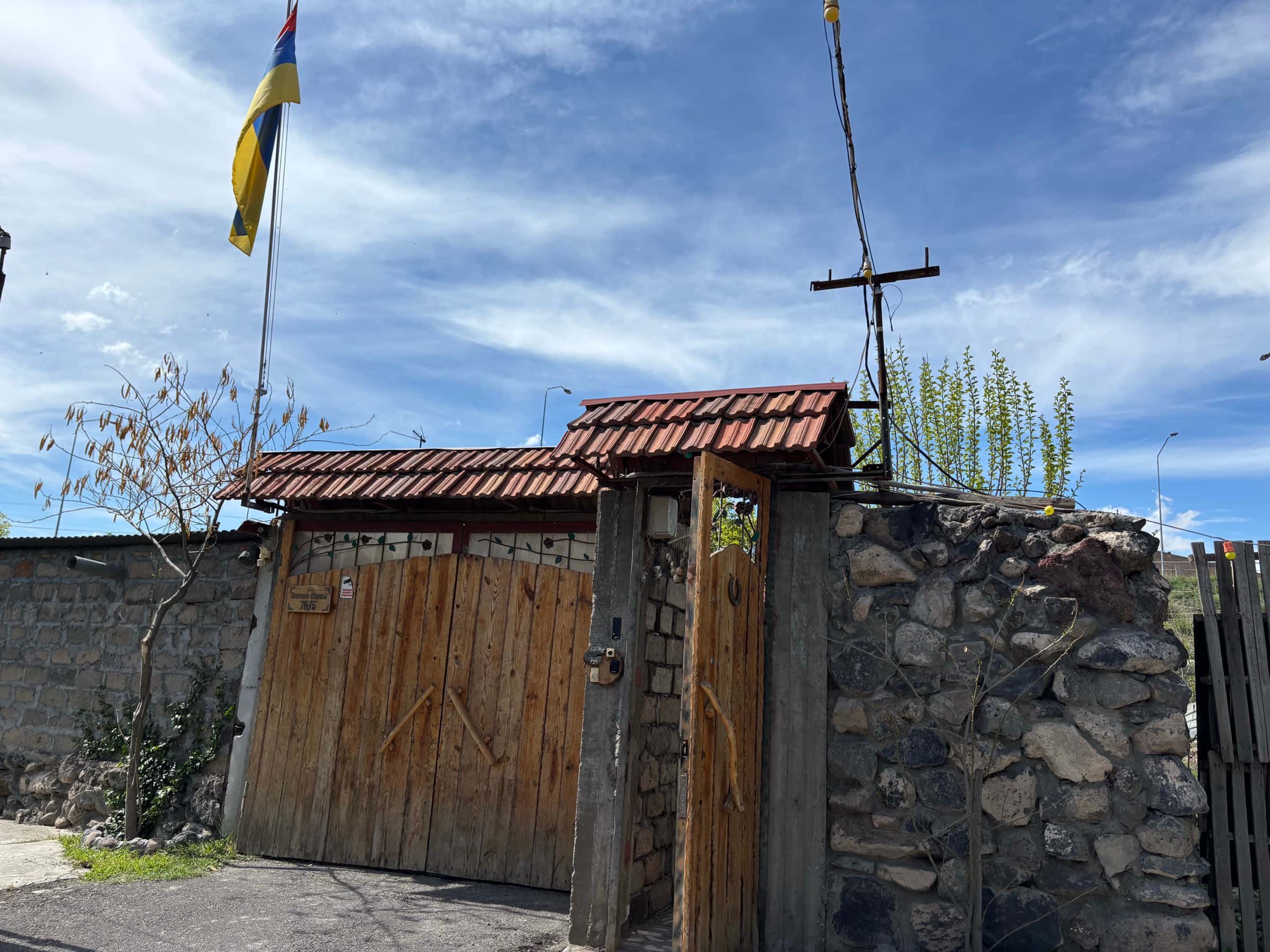 Villa Nors-ի փայտե երկփեղկ դարպասը՝ կղմինդրե ծածկով, հայկական դրոշով և քարե պարսպով